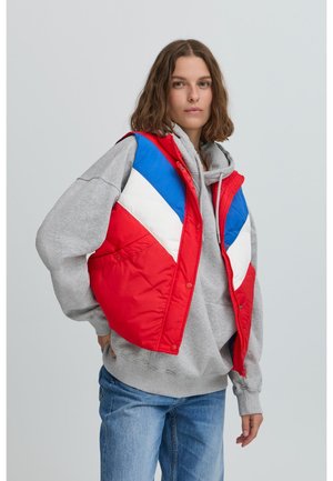 Rote und blaue gepolsterte Weste mit einem Chevron-Muster und weißen Akzenten, getragen über einem grauen Kapuzenpullover. Das Material erscheint glatt mit einer glänzenden Oberfläche.