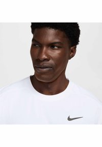 Balta Nike marškinėliai su apvalia iškirpte ir trumpomis rankovėmis. Puošia sidabrinis logotipas kairiajame krūtinės šone ir tekstūruotas audinio dizainas.