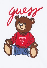Tecknad björngestalt i röd tröja med en triangelformad "GUESS?"-logotyp och jeanjacka, mot en vit bakgrund.