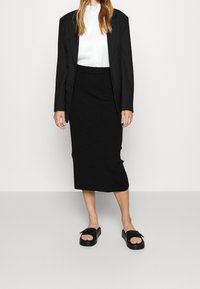 Černá žebrovaná midi sukně v kombinaci s černým oversized blejzrem a bílým topem, doplněná černými sandály s detaily na přezku.