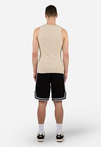 Beige ribbet tank topp og svarte shorts med hvite striper i kanten. Modellen vist bakfra, iført hvite sokker og svarte sko.