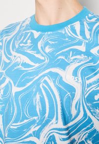 Close-up of a person wearing a blue crewneck shirt with a white abstract swirl pattern and the word "BOSS" on the chest.