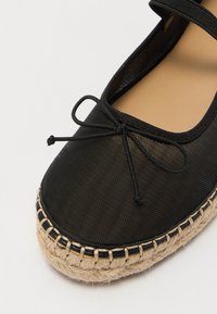 Espadrillas nere con tomaia in tessuto intrecciato, caratterizzate da un dettaglio con fiocco e una suola intermedia in corda di juta. Fodera interna liscia. Punta arrotondata.