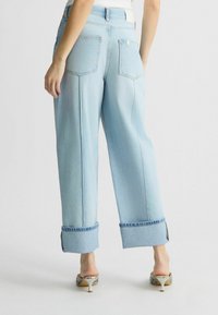 Jeans largi cu talie înaltă, de culoare albastru deschis, cu mansete răsucite, având buzunare mari aplicate și detalii cu cusături contrastante.