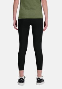 Leggings neri con un design aderente, realizzati in tessuto elasticizzato, abbinati a scarpe da ginnastica, visti da dietro. Semplici e funzionali.