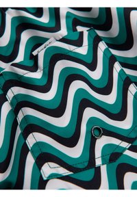 Gros plan sur un tissu avec des rayures ondulées turquoise, noires et blanches et une poche à rabat cousue avec un petit bouton rond.