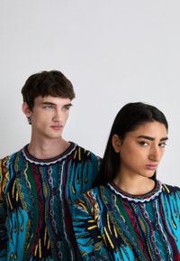 Knit sweaters featuring colorful, abstract patterns in blue, red, and yellow with round necklines and textured fabric.
