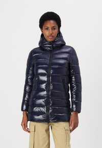 Marineblauwe gewatteerde jas met een hoge kraag, glanzende textuur, voorrits en twee zijzakken. Heeft gestikte horizontale naden.