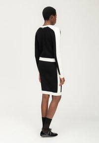 Schwarzes und weißes gestricktes Kleid mit langen Ärmeln, das kontrastierende Seitenpaneele und eine taillierte Silhouette aufweist. Glatte Textur und knielang.