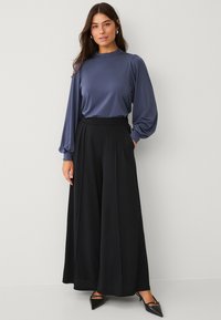 Blauwe blouse met lange mouwen en pofschouders, gecombineerd met hoge zwarte wijde broek en puntige zwarte instappers. Gladde stofstructuur.