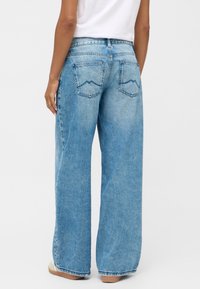 Jasnoniebieskie dżinsy typu wide-leg z wysokim stanem, z dwoma tylnymi kieszeniami z wzorem ściegu w zygzak i surowym wykończeniem. Wykonane z materiału dżinsowego.