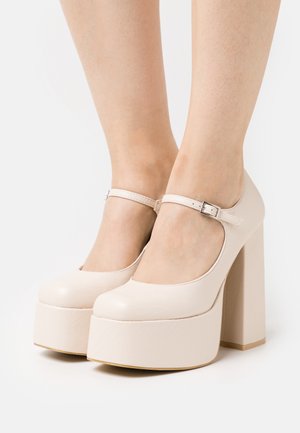 Talons Mary Jane à plateforme beige avec un bout arrondi, une bride réglable à la cheville et des talons épais en bloc, présentant un similicuir à texture lisse.