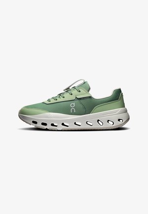Chaussure de course basse verte avec semelle blanche comportant des découpes ovales et des dessins latéraux marqués.