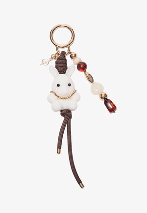 Nøglering med en hvid kaninf figur lavet af blødt materiale, detaljer i guldfarvet kæde og dekorative perler i brune og ravfarvede nuancer.