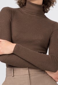 Bruine geribbelde turtleneck trui, nauwsluitend ontwerp, lange mouwen, zachte textuur, gecombineerd met lichtbeige high-waisted broeken.