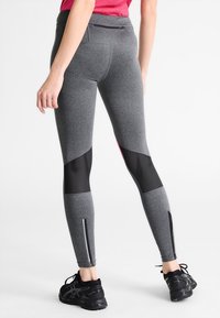 Harmaat urheiluleggingsit, joissa on korkea vyötärö, verkkoaksentit ja vetoketjullinen tasku. Ominaisuuksiin kuuluu heijastava yksityiskohta ja tiukka muotoilu.