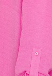 Rosa Hemd mit Knöpfen aus strukturiertem Stoff. Verfügt über einen runden Kragen und einen einzelnen Knopf am Ärmel, der ein dezentes Fischgrätmuster zeigt.