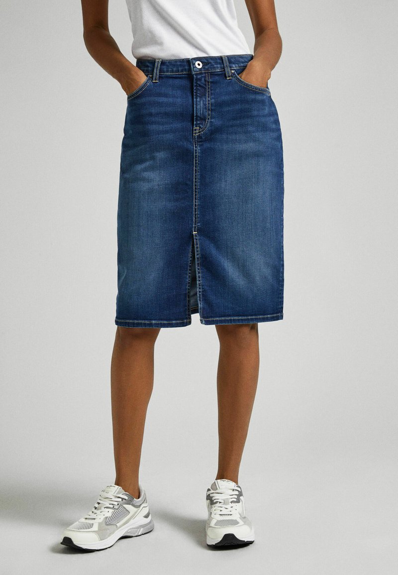 Denim midi skirt in dark blue, featuring front pockets, a central split seam, and a classic button closure. Paired with white and gray sneakers.