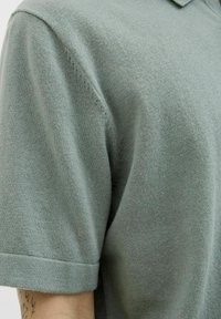 Polo shirt vert clair en tissu doux, doté d'un col classique et de manches courtes avec une texture lisse et des détails de couture minimalistes.