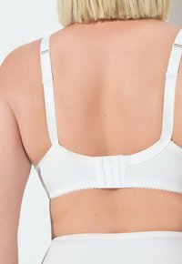 Witte beha met verstelbare bandjes, gladde textuur, haak-en-oogsluiting aan de achterkant en gegolfde randdetails langs de band.