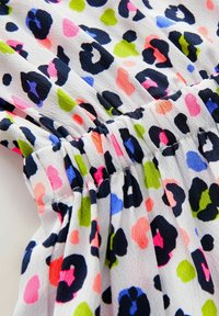 Tissu en impression léopard avec des taches multicolores en rose, vert, bleu et noir ; texture froncée le long de la couture. Matériau doux et léger.