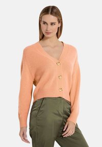 Licht koraalkleurige gebreide cardigan met een V-hals, voorzien van vier gouden knopen aan de voorkant en geribde mouwen, gecombineerd met olijfgroene broek.