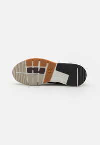 Schwarze Sneaker-Sohle mit gerilltem weißen Gummi, versehen mit orangefarbenen und lila Akzenten. Größe 42 auf dem weißen Gummipanel gekennzeichnet. Texturierte Oberfläche.