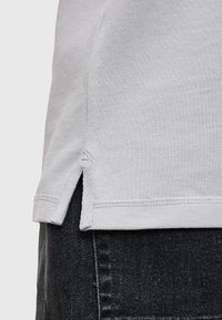Lichtgrijs shirt met korte mouwen, voorzien van een textuur, zijsplitten en versterkte stiksels langs de zoom, gecombineerd met een donkere spijkerbroek.
