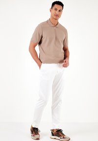 Bēša īsām piedurknēm polo krekls ar rāvējslēdzēju apkaklī, saskaņots ar baltām šaurām biksēm un daudzkrāsainām sporta kedām ar melnā un brūnā akcentiem.