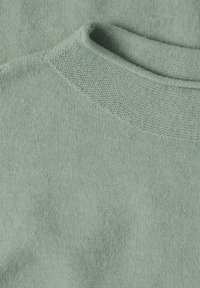 Gros plan d'un pull tricoté vert clair présentant son col rond et son motif en maille texturée.