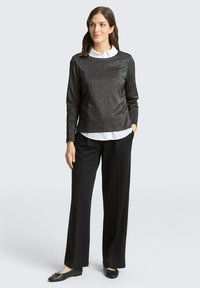 Czarna, błyszcząca bluzka z długim rękawem nałożona na białą koszulę z kołnierzykiem, zestawiona z czarnymi spodniami w paski i czarnymi balerinami. Gładka faktura, swobodny krój.