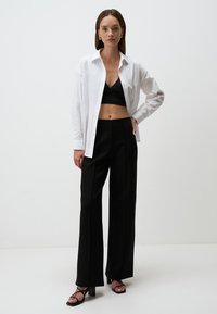 Chemise blanche à boutons, top court noir, pantalon large noir, et talons noirs avec lanières. Design simple et épuré avec une silhouette ajustée.