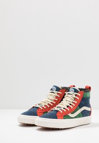 Baskets montantes en daim bleu, rouge et vert, lacets blancs, et col rembourré rouge. Tige texturée avec des accents latéraux blancs.