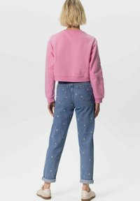 Sweatshirt rose à manches longues et coupé court, associé à un jean bleu clair avec des motifs floraux brodés et des poignets roulés. Chaussures décontractées comprises.