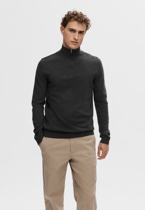 Dark gray quarter-zip sweater with long sleeves and ribbed cuffs, paired with beige pants. Simple design, smooth knit texture.