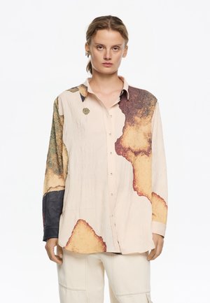 Camisa de manga larga y botón en un beige claro con patrones abstractos en marrón y verde. Hecha de un tejido texturizado con un aspecto ligeramente arrugado.