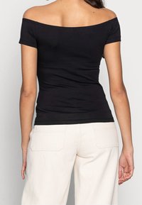 Svart off-shoulder-top med korta ärmar; figurnära design; mjukt tyg; kombinerad med ljusa, högmidjade byxor med bakfickor.