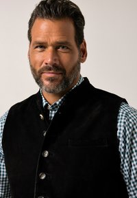 Gilet di suede nero con bottini d'argento, indossato sopra una camicia a quadretti verdi e bianchi. Collo alto e taschino singolo sul gilet.