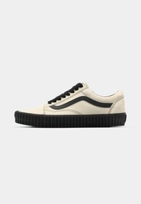 Zapatillas de lona beige con suela de goma negra, cordones negros y detalle de franja lateral. Superficie texturizada con un diseño estilizado.