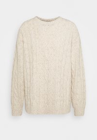 Krämfärgad stickad tröja med kabelstickat mönster, rund halsringning och ribbade avslut på ärmar och nederkant. Mjuk textur med en avslappnad passform.