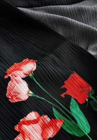 Zwart geplooid stof met rode en roze rozenpatronen, gelaagd over een grijze gestructureerde achtergrond, die de bloemendetails en contrasterende kleuren benadrukt.