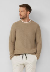 Brauner, gerippter Strickpullover mit Rundhalsausschnitt und überschnittenen Schultern, kombiniert mit hellen Cargo-Hosen mit Kordelzugdetails.