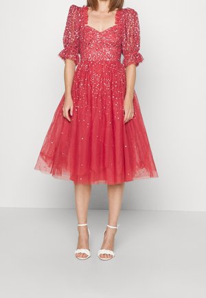 Rode tulejurk met glinsterende applicaties, pofmouwen en een getailleerde taille. Gecombineerd met witte sandalen met bandjes en een zoom tot op de knie.