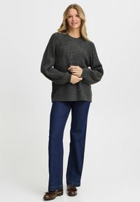Dunkelgrauer, gerippter Strickpullover mit Rundhalsausschnitt und langen Ärmeln, kombiniert mit dunkelblauen Schlagjeans und braunen Schuhen.