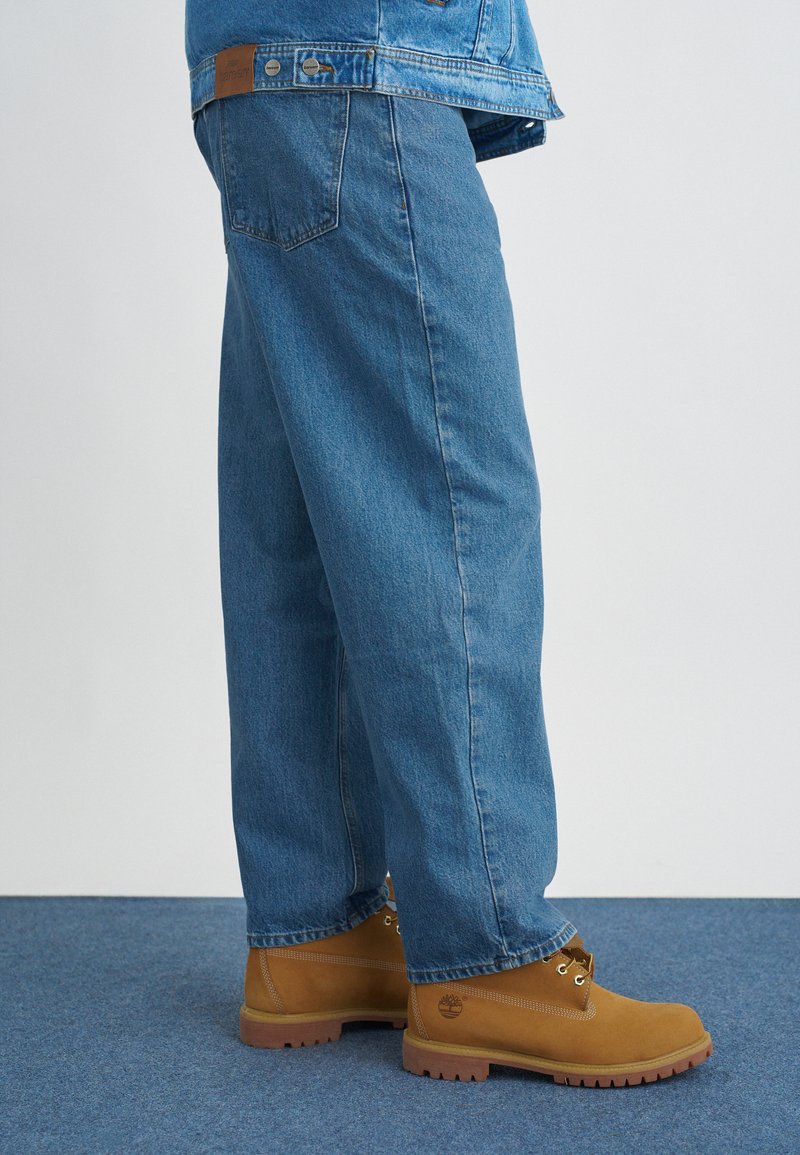 Calças de ganga azul claro com um corte relaxado, combinadas com botas de tornozelo bege com ilhós de metal e uma sola texturizada.