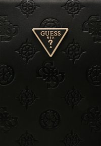 Superficie in pelle nera con motivi in rilievo; presenta un logo triangolare dorato etichettato "GUESS USA" al centro.