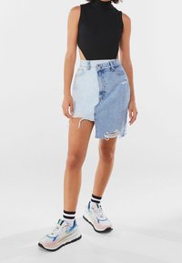 Denim-hame, jossa puolen vaalean ja puolen keskitumman pesun yhdistelmä ja rispaantunut helma; yhdistetty mustaan hihattomaan bodysuitiin ja tukevasti paksupohjaisiin tennareihin.