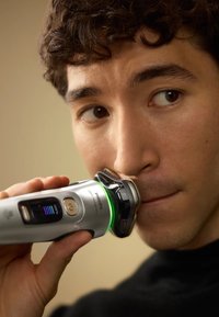 Philips elektrische scheerapparaat met een zilveren body, zwarte accenten, LED batterij-indicator en groen licht, dat wordt gebruikt op de huid nabij de mond.