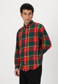 Camicia a quadri rossa, verde e gialla con colletto e maniche lunghe. Presenta una tasca sul petto e una vestibilità comoda.