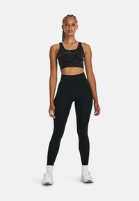Zwarte cropped sport-bh met een camouflagedessin en hoge zwarte leggings. Het model draagt witte sneakers en enkelsokken.